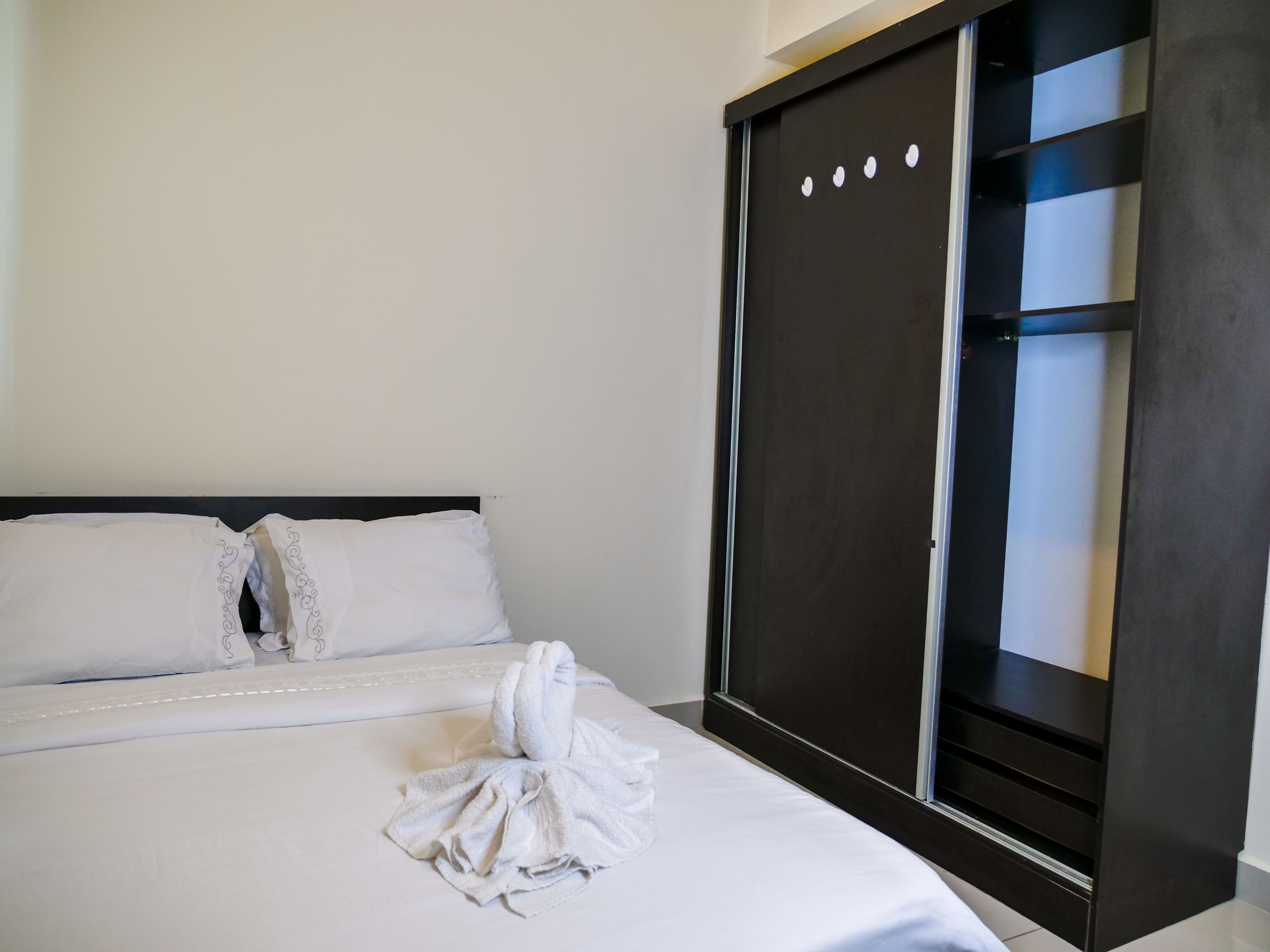 A hotel room with a bed, white linens, a dark-colored wardrobe, and a large window.