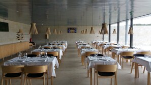 A restaurant with tables set for dining, a long counter, and a view of the water.