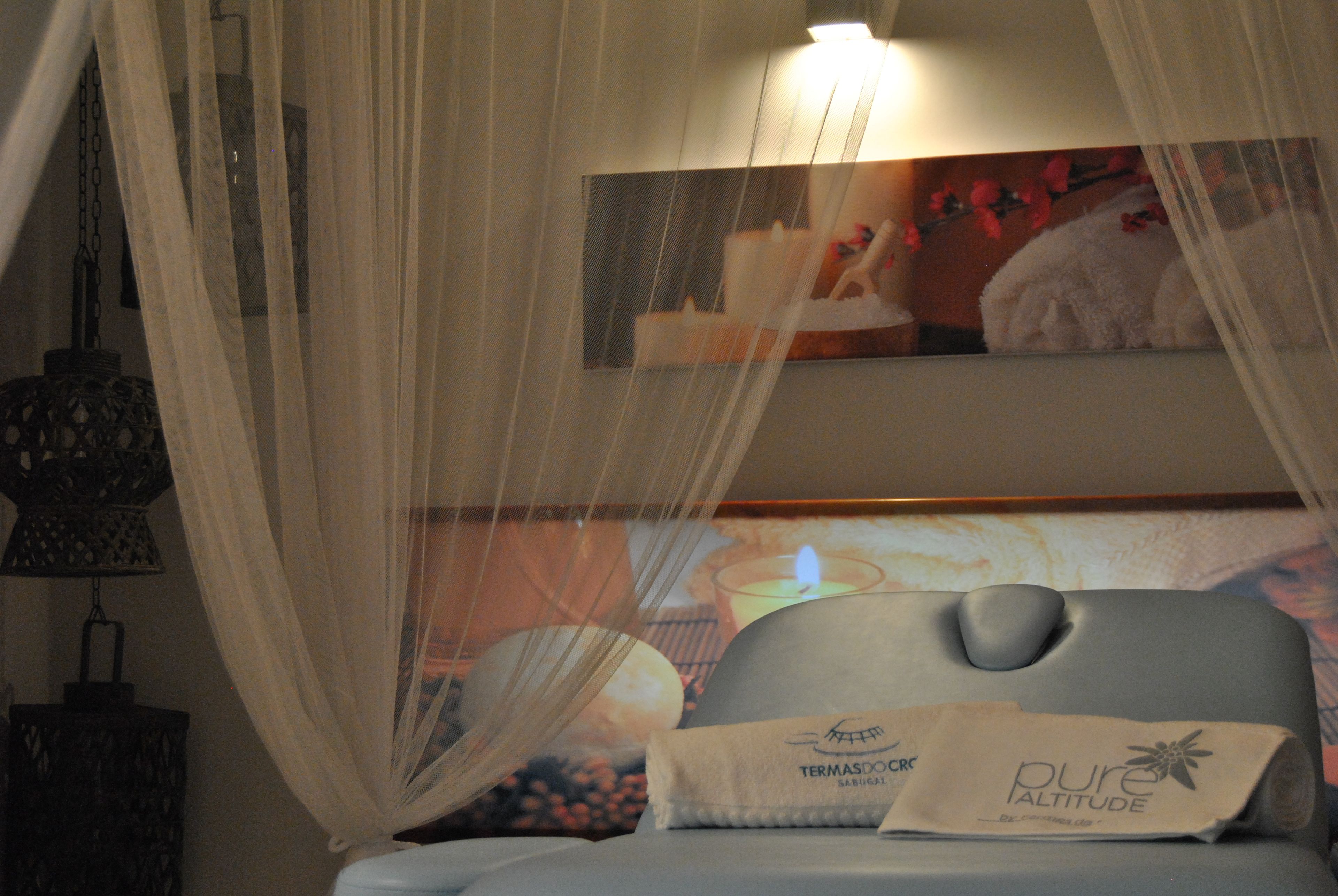 A bed with a canopy, a pillow with 'Pure Altitude' branding, and a wall-mounted lamp.