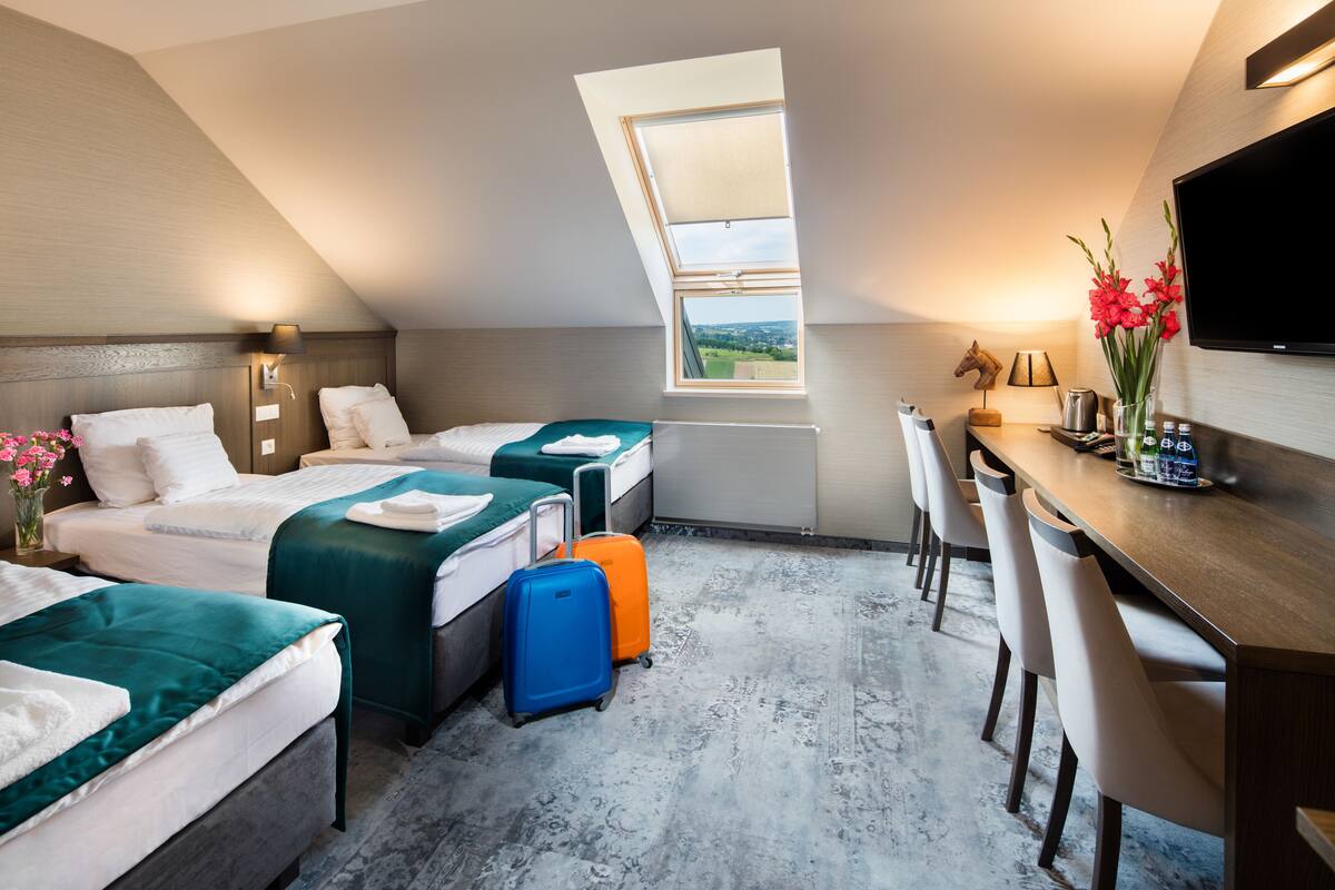 Quarto de hotel com duas camas, uma escrivaninha, televisão e claraboia.