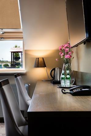 A hotel room with a wooden table, two chairs, a vase with pink flowers, a lamp, and a kettle. - Hotel Szary Residence (Michalowice)