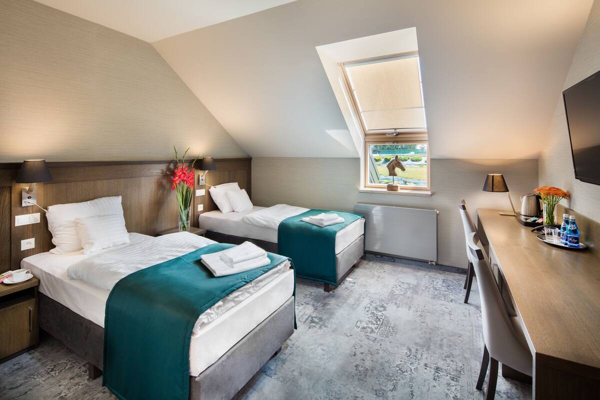 Quarto de hotel com duas camas, uma escrivaninha e uma janela com vista para o verde.