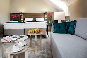A hotel room with two beds, a sofa, a small round table with two cups of coffee and a fruit bowl, and a magazine on the table. - Hotel Szary Residence (Michalowice)
