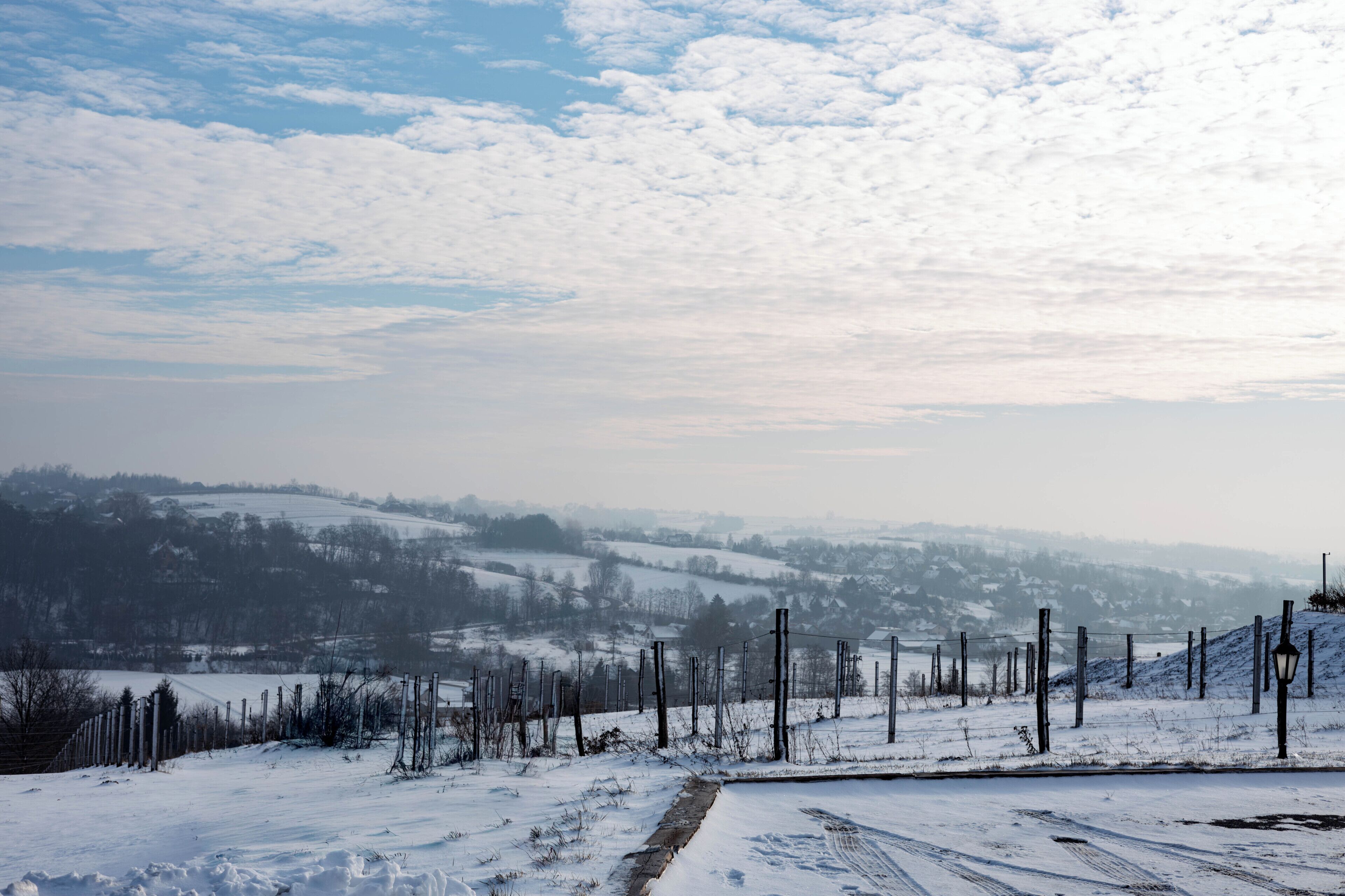 A snowy landscape with a clear sky, a fence, and a road leading into the distance.