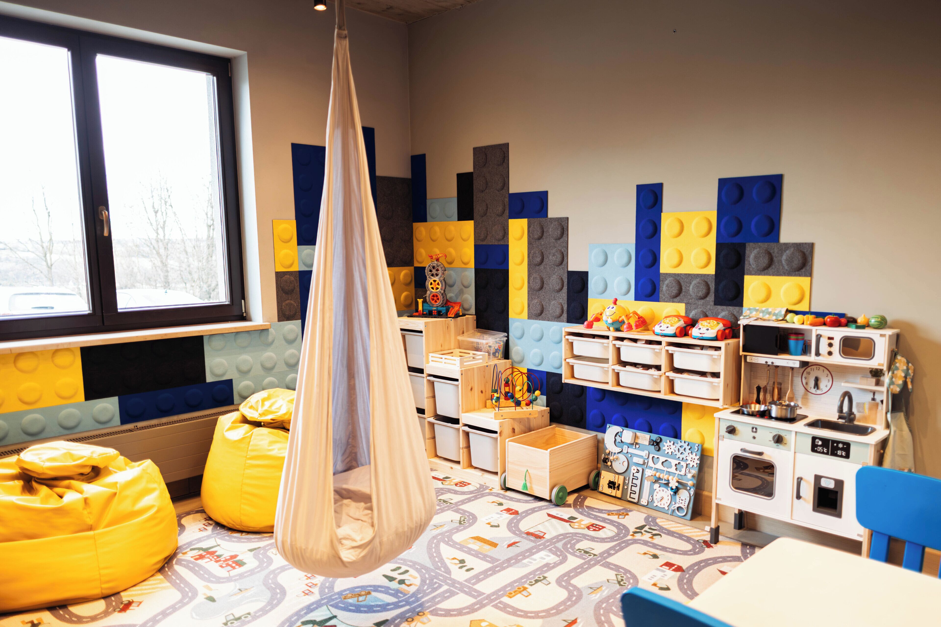 Ein Kinderzimmer mit Hängekorbschaukel, Stauraumelementen und einem Fenster.