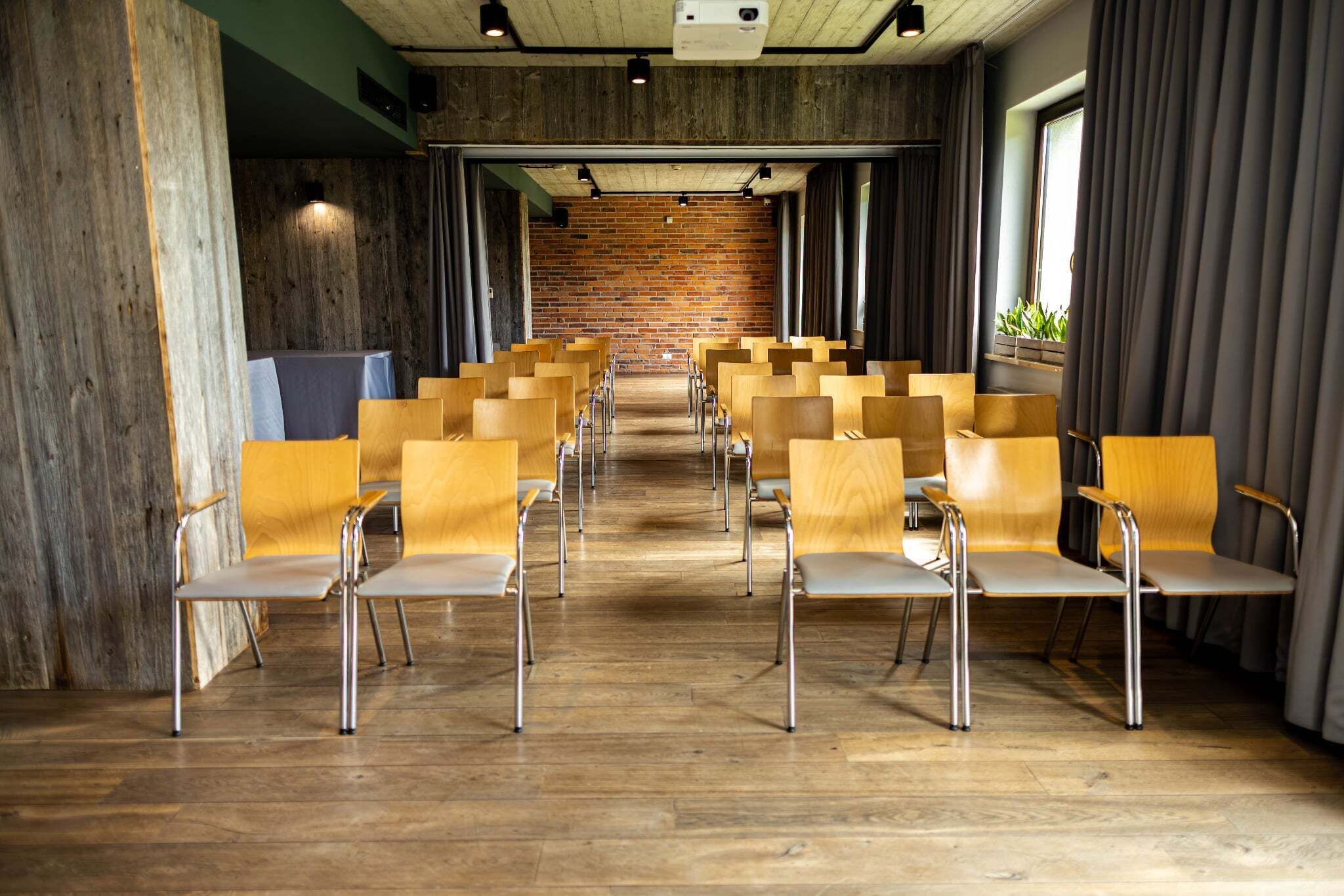 Un salón de conferencias con filas de sillas de madera, una pared de ladrillo y suelo de madera.