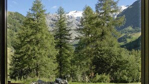 Une terrasse avec un fauteuil à bascule, une zone pavée et une vue sur un paysage montagneux, avec des arbres et une route.