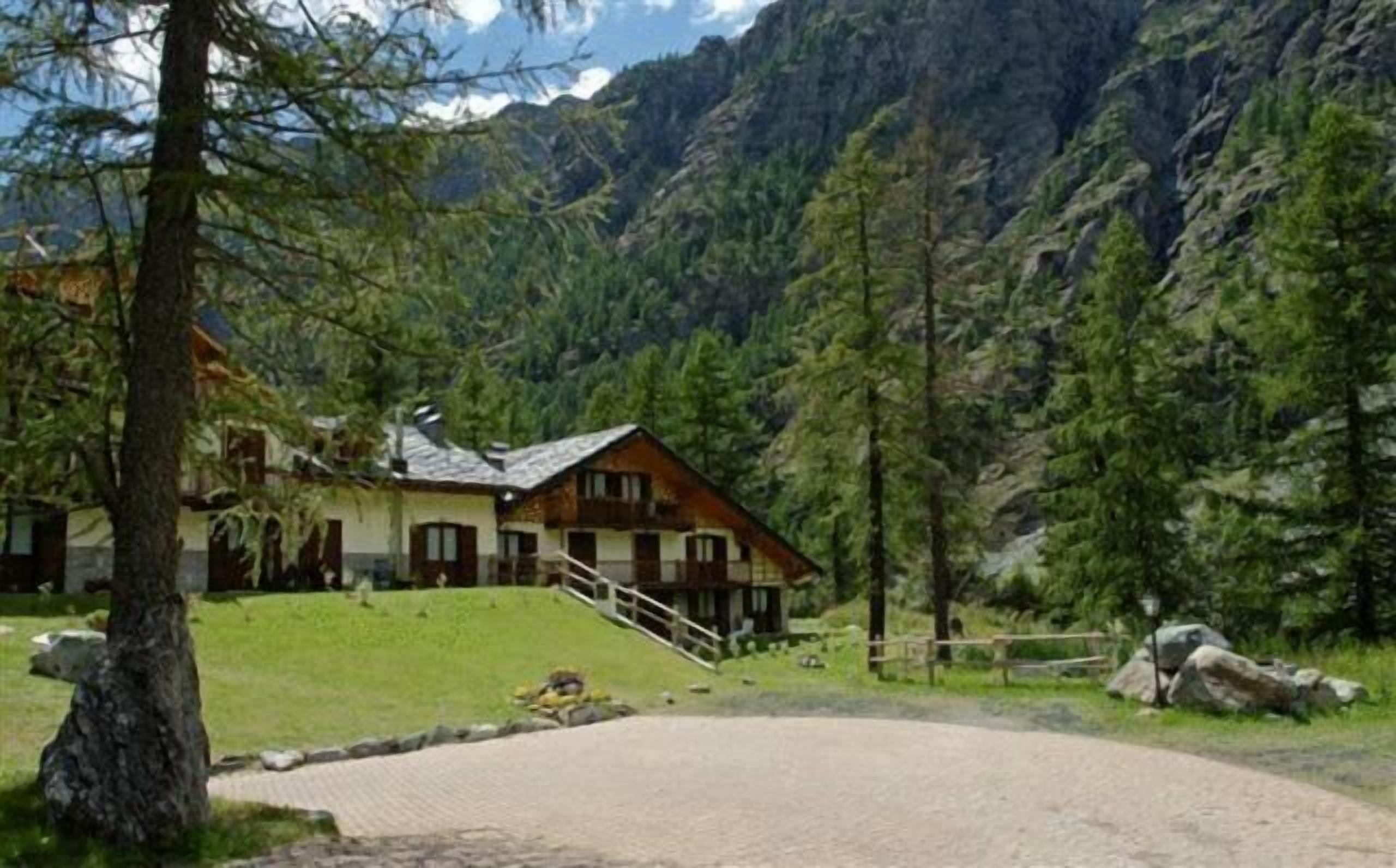A lodge with a stone staircase leading to a wooden deck, surrounded by lush greenery and mountains.