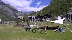 Une zone montagneuse avec une aire de jeux, des tables de pique-nique et des bâtiments en arrière-plan.