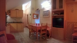 Une cuisine compacte avec des meubles en bois, une table à manger avec des chaises, un téléviseur et un petit coin salon avec un canapé rouge.