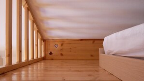 Une chambre mansardée en bois, avec un plafond en pente, un lit et une petite décoration en forme de cœur accrochée au mur.