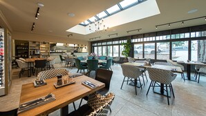 A modern restaurant with high ceilings, large windows, and a variety of seating arrangements.