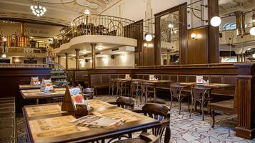A restaurant with a high ceiling, ornate railings, and a central staircase. Tables are arranged with menus and condiments.