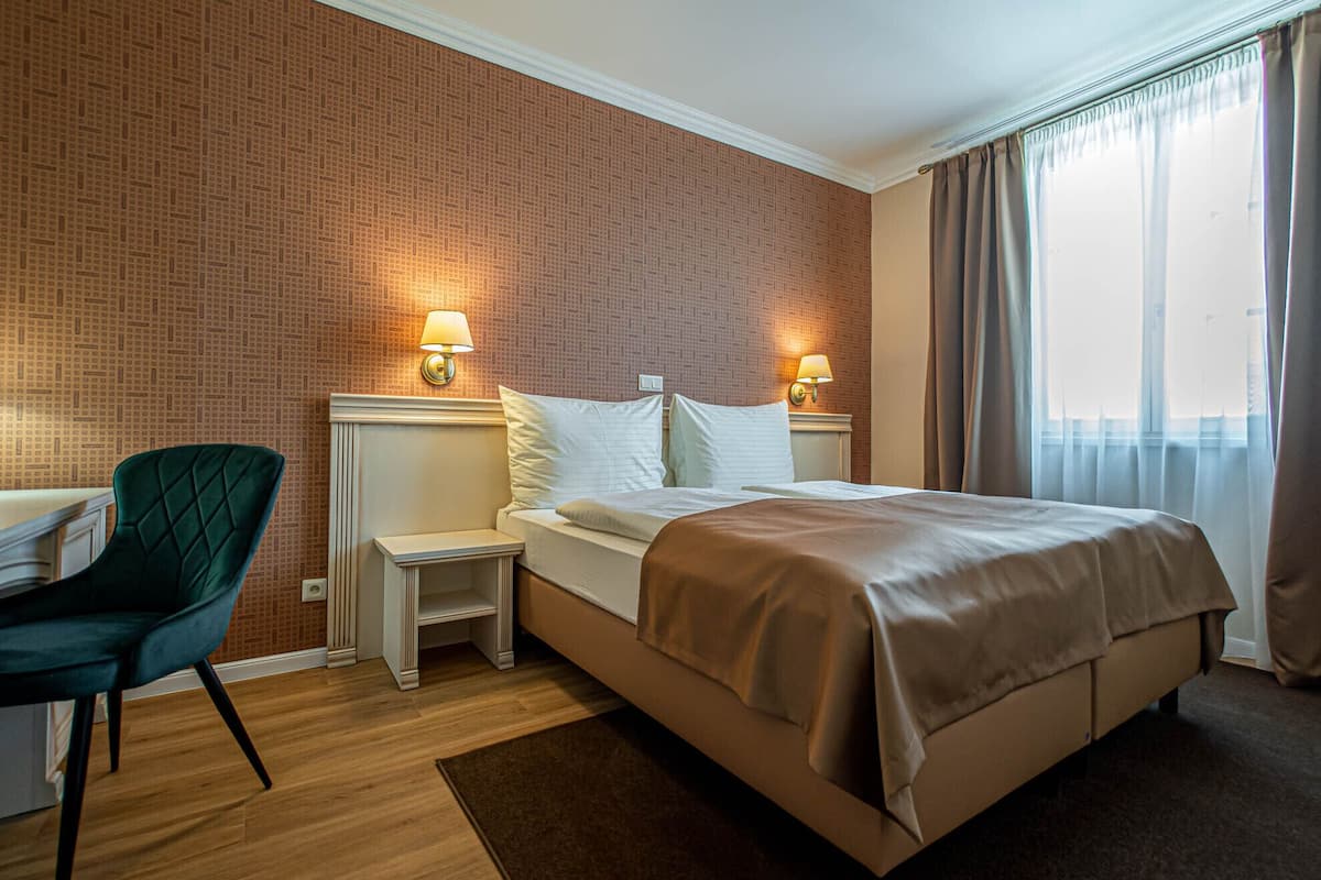 A hotel room with a bed, two bedside tables, a chair, and a window with curtains.