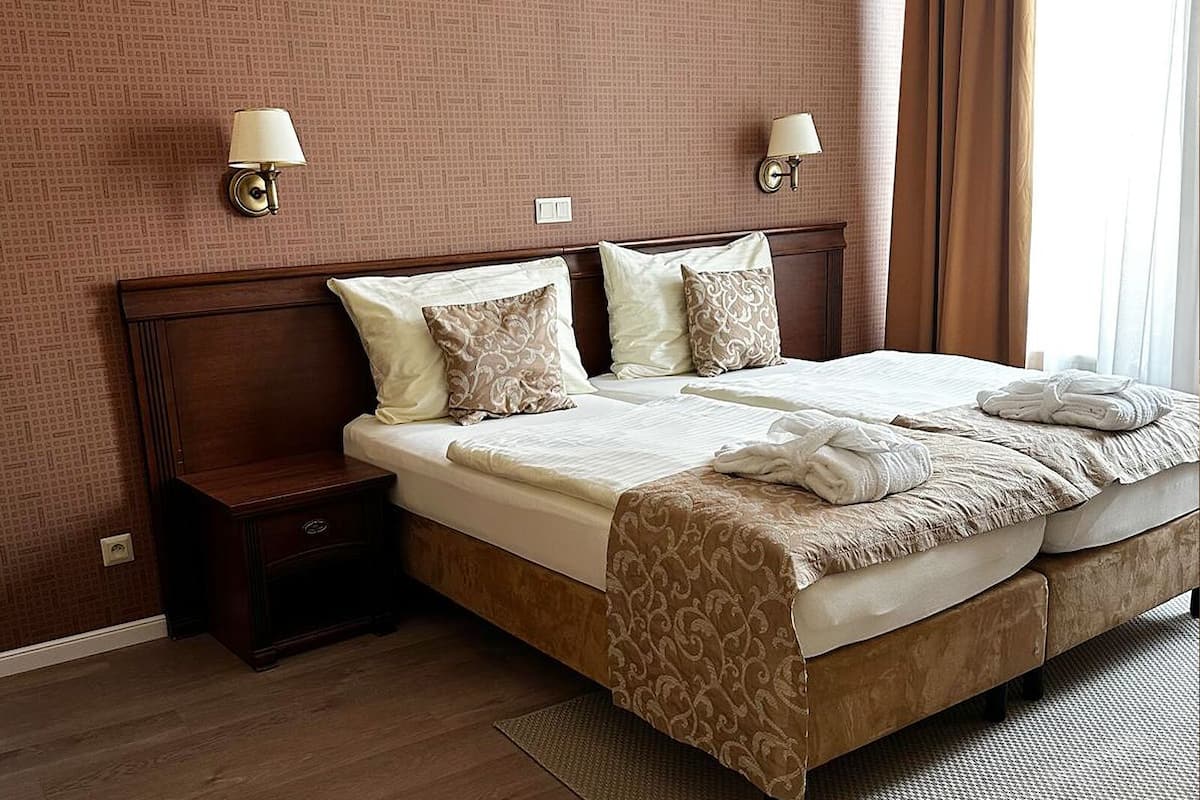 A hotel room with a large bed, two bedside tables, and two wall-mounted lamps.