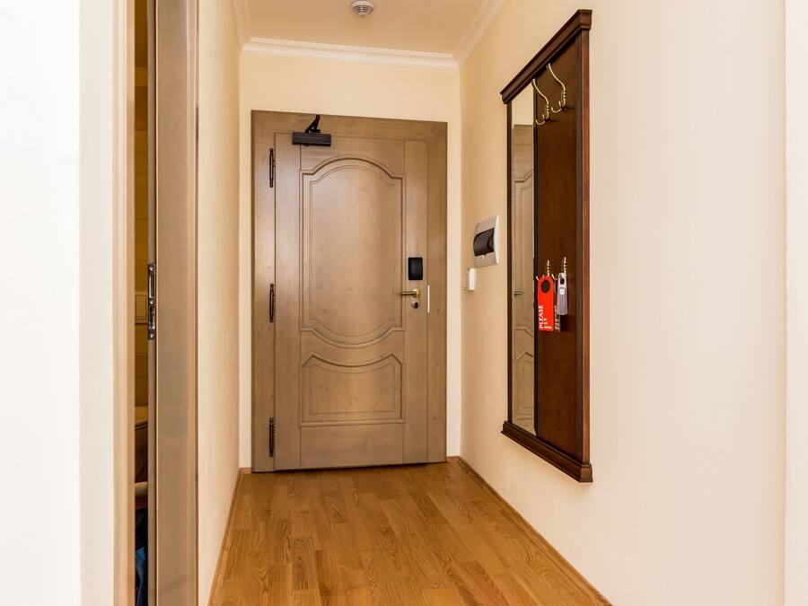 A hallway with a wooden door, a mirror on the wall, and a fire extinguisher.