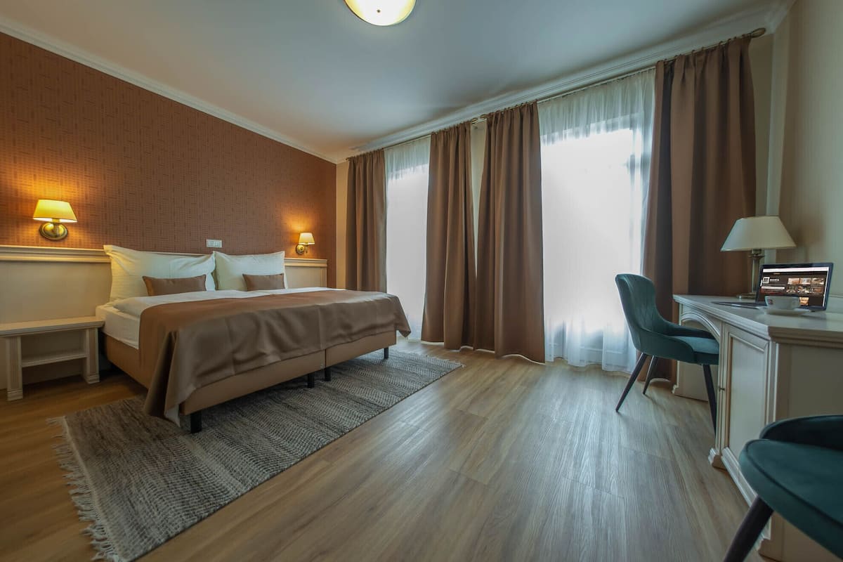 A hotel room with a bed, desk, chair, and two wall-mounted lamps.