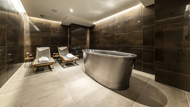 A modern bathroom with a freestanding bathtub, a wooden bench, and a mirror.