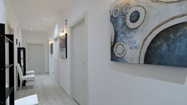 A hallway with white walls, a large abstract painting, and a white bench. - Town House 57 (Rome)