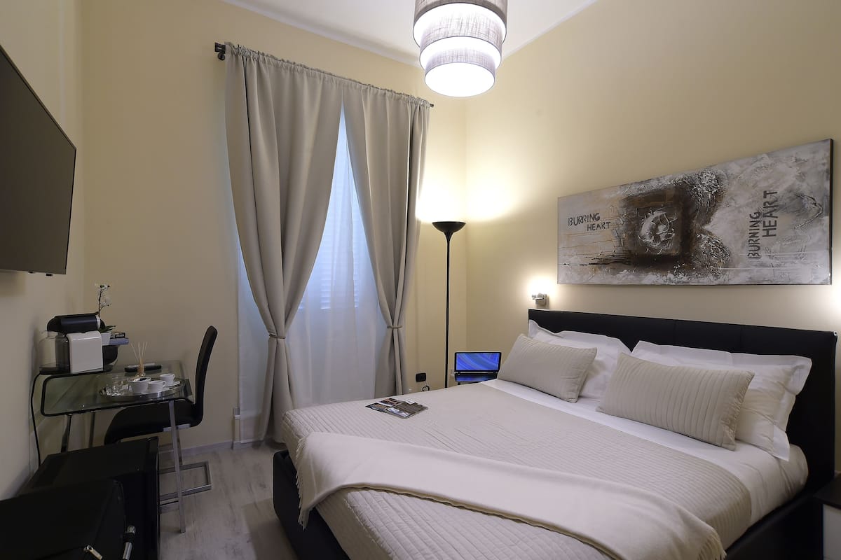 A neatly arranged hotel room with a bed, a desk with a computer, a lamp, and a painting on the wall.