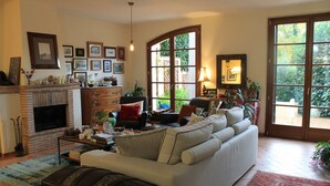 A living room with a fireplace, sofa, and large windows. - Donna Etrusca B&B (Sutri)