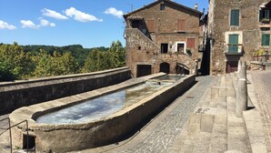 A stone water well with a stone staircase leading up to a building with a traditional stone facade and wooden shutters. - Donna Etrusca B&B (Sutri)