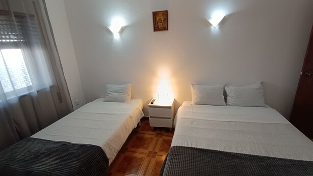 A twin room with two beds, a nightstand, a wall-mounted light, and a window with curtains. - Residencial S. Gião (Valenca)