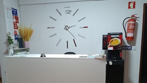 A reception desk with a clock, a Nescafé coffee machine, a fire extinguisher, and a sign that reads "RECEPCÃO". - Residencial S. Gião (Valenca)
