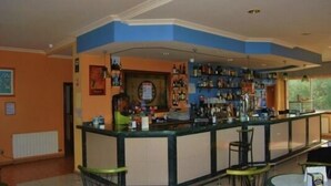 A bar area with a counter, shelves of bottles, and bar stools. - Hostal O Rancheiro (Vigo)