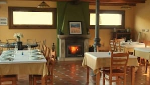 A dining area with tables set for two, a fireplace, and a view of the outdoors. - Hostal O Rancheiro (Vigo)