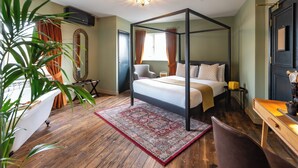 A bedroom with a four-poster bed, a desk, a chair, a plant, and a large window with curtains. - Bear Hotel (Bath)