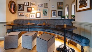 A seating area with a curved bench, three square ottomans, and three round tables. - Bear Hotel (Bath)
