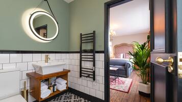 A bathroom with a white sink, a mirror with a light, a towel rack, and a wooden shelf with towels.