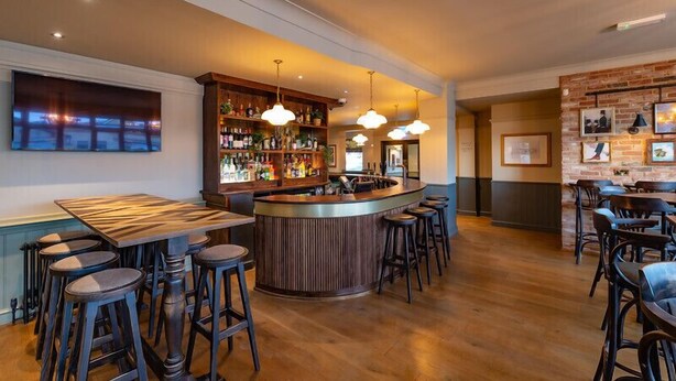 A bar area with a wooden bar counter, stools, and hanging pendant lights. - Bear Hotel (Bath)