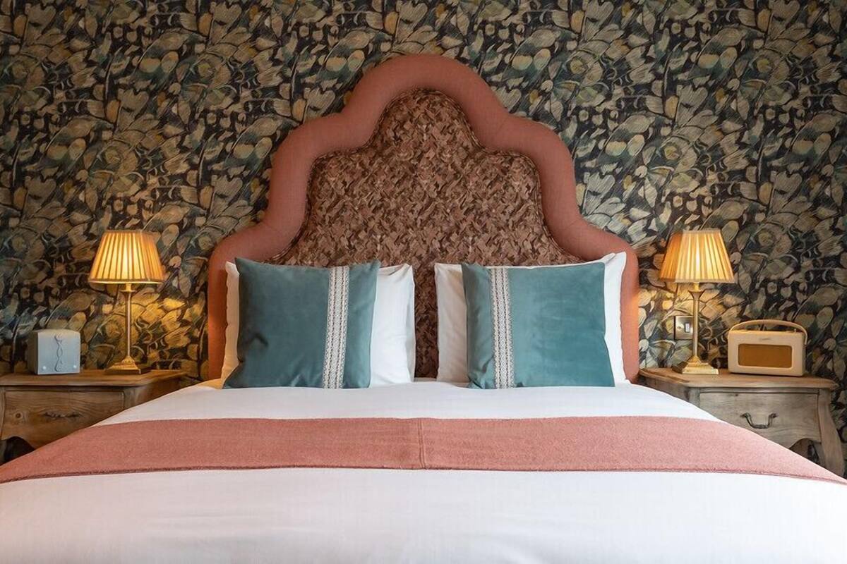 A bed with a woven headboard, two bedside lamps, and a patterned wallpaper.