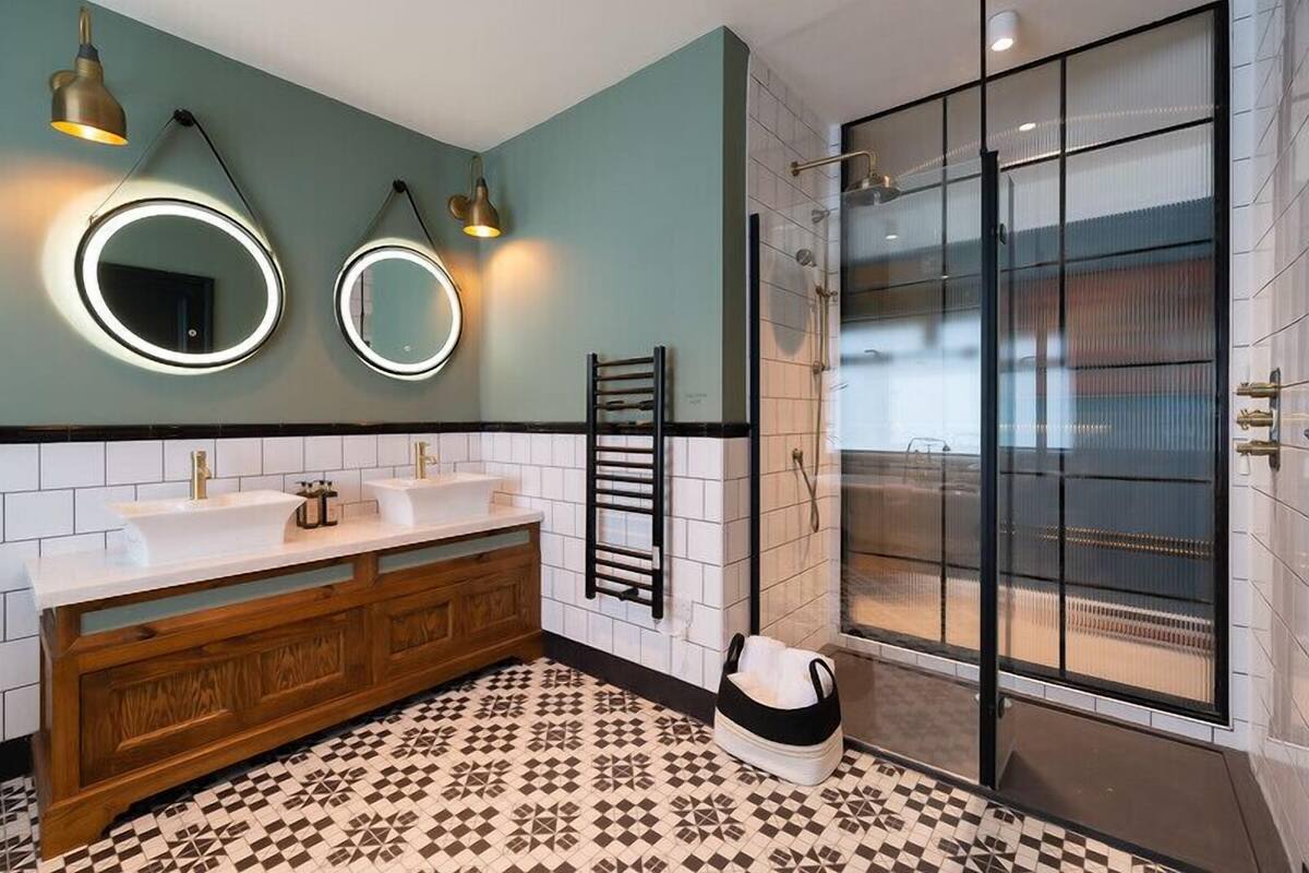 A modern bathroom with two sinks, a wooden vanity, a towel rack, and a glass shower enclosure.