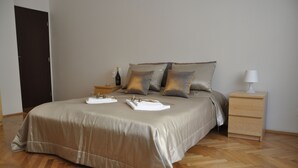 A neatly made bed with a beige bedspread, two pillows, and a nightstand with a lamp and a bottle. - Metropolis Prague Apartments (Prague)