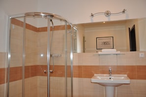 A bathroom with a glass-enclosed shower, a sink, and a framed picture on the wall.