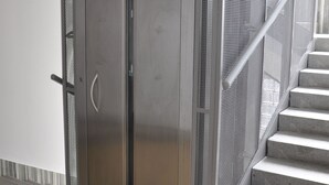 A metallic elevator with a mesh safety guard, adjacent to a staircase with a metal railing. - Metropolis Prague Apartments (Prague)