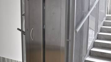 Ein metallener Aufzug mit einem Drahtgitter-Schutzgitter neben einer Treppe mit Metallgeländer.