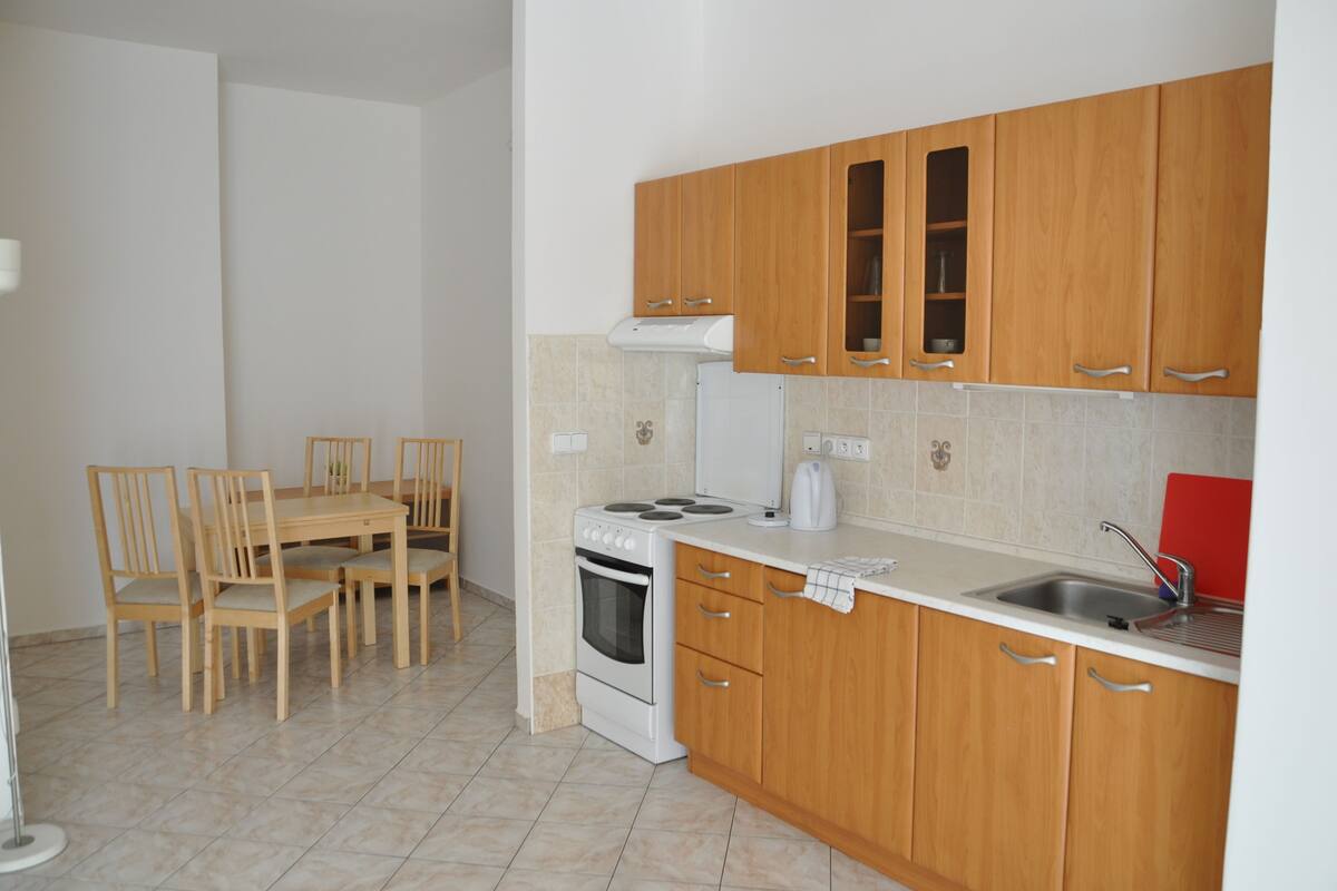 A kitchen with wooden cabinets, a stove, a sink, and a dining area with chairs.