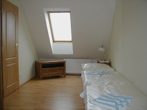 Een slaapkamer met een schuine kap, een dakraam, een houten nachtkastje, een bed met witte beddengoed, en een radiator.