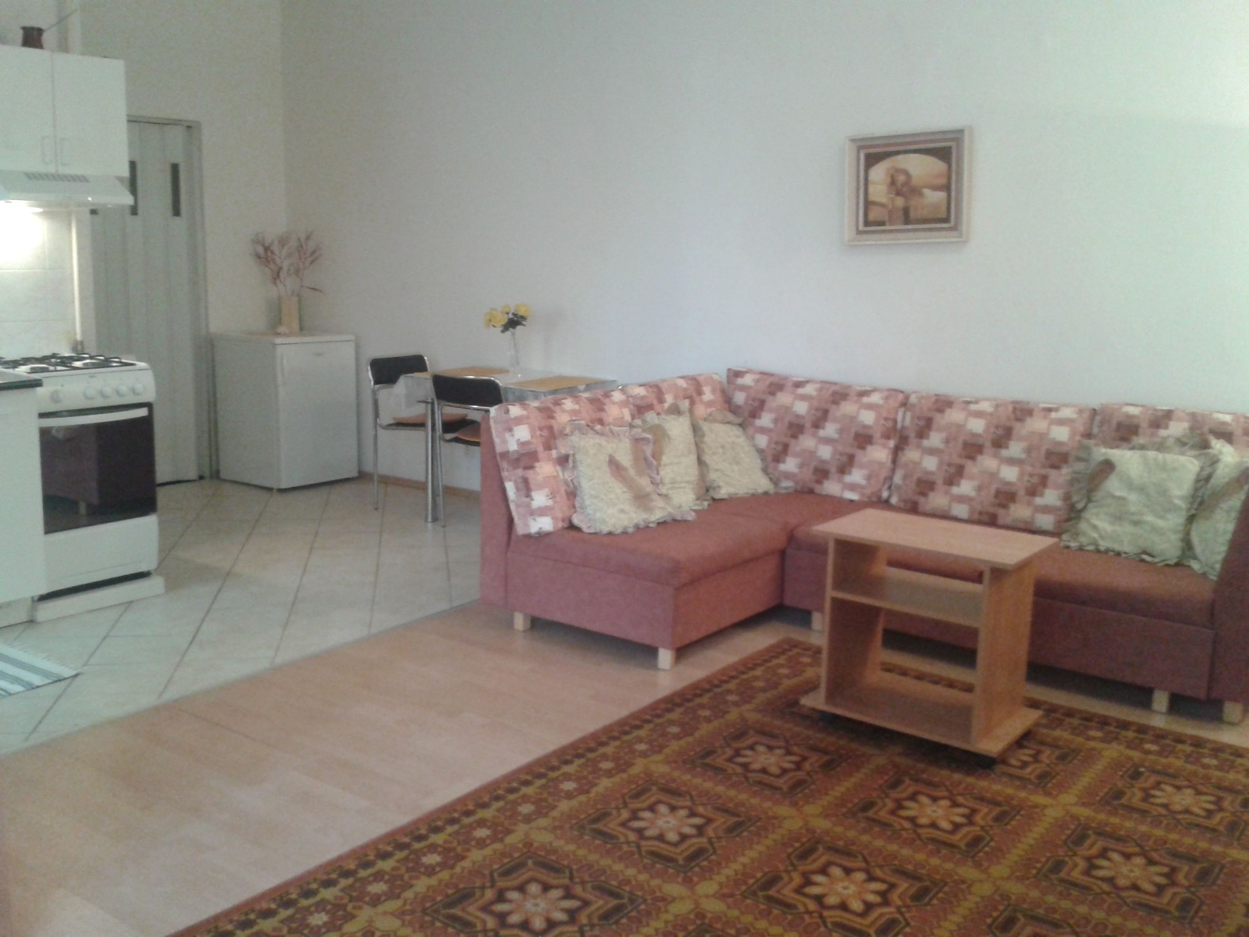 A living room with a sofa, a small table, a kitchen area with a stove, and a refrigerator.