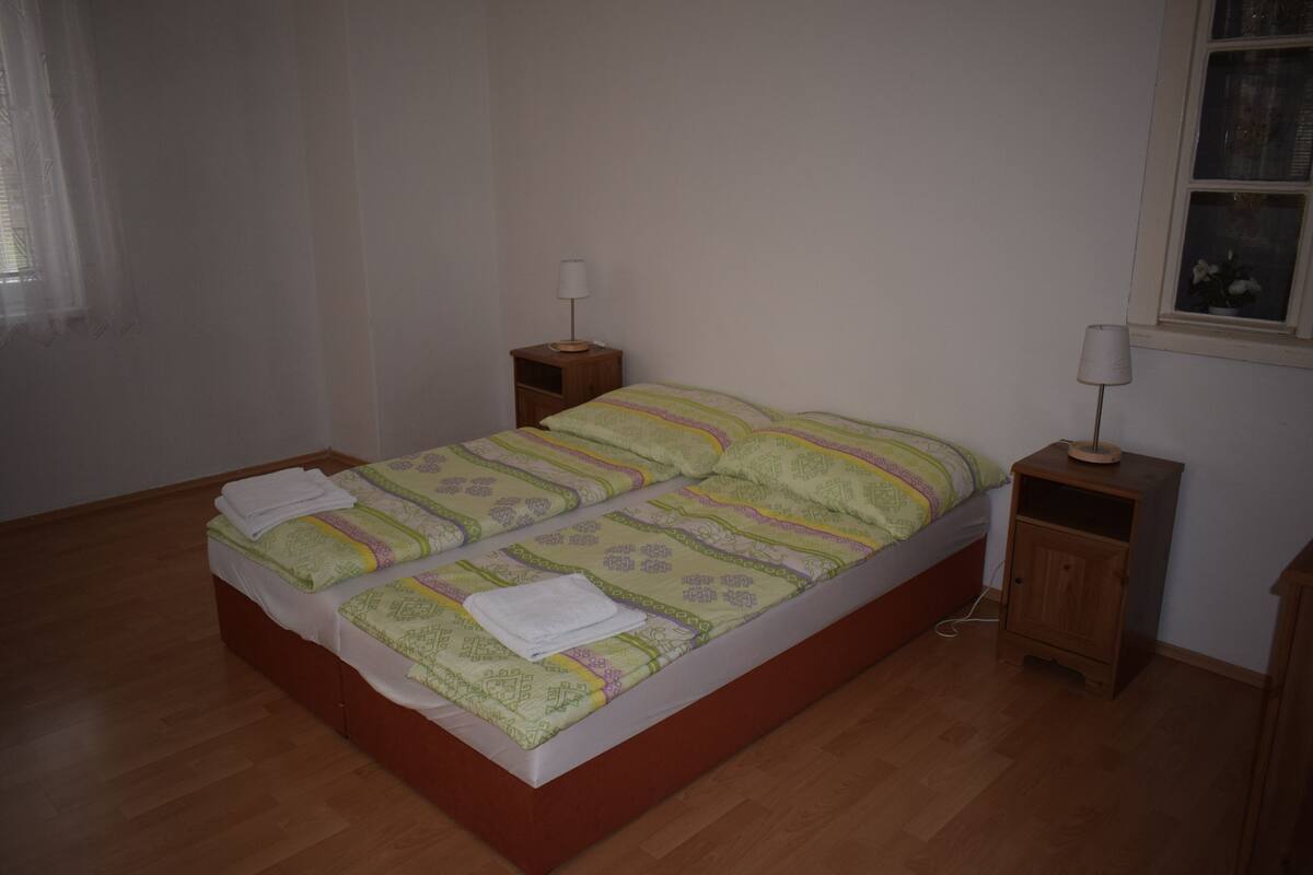 A neatly made bed with a patterned bedspread, two bedside tables with lamps, and a window with a view.