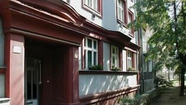 A building with a red facade, a visible entrance, and a small garden area. - Apartmany Bratislava (Bratislava)