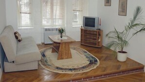 A living room with a sofa, a coffee table, a television on a wooden stand, and a potted plant. - Apartmany Bratislava (Bratislava)