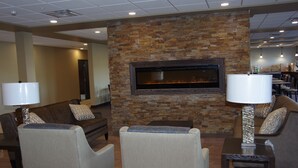 A lobby with a stone wall and a fireplace, seating area with couches and chairs, and a dining area in the background.