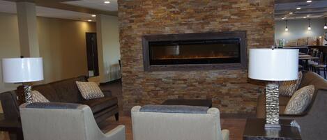 A lobby with a stone wall and a fireplace, seating area with couches and chairs, and a dining area in the background.