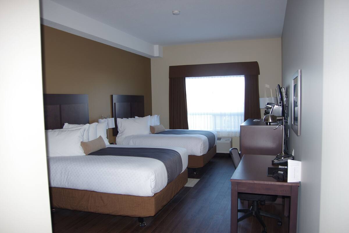 Ein Hotelzimmer mit zwei Betten, einem Schreibtisch, einem Stuhl, einem Fernseher und einem Fenster mit Vorhängen.