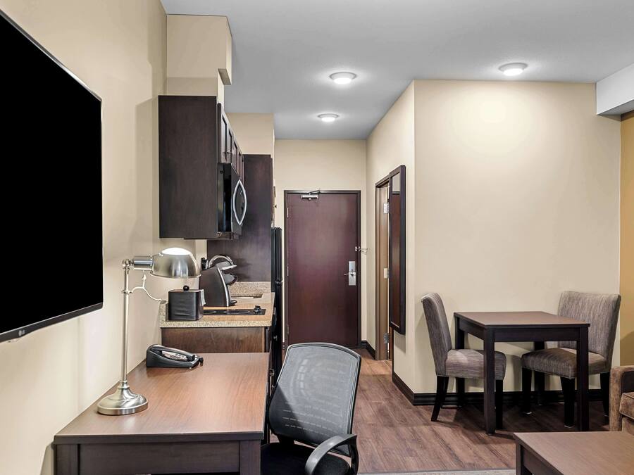 A hotel room with a desk, chair, table, and a flat-screen TV.